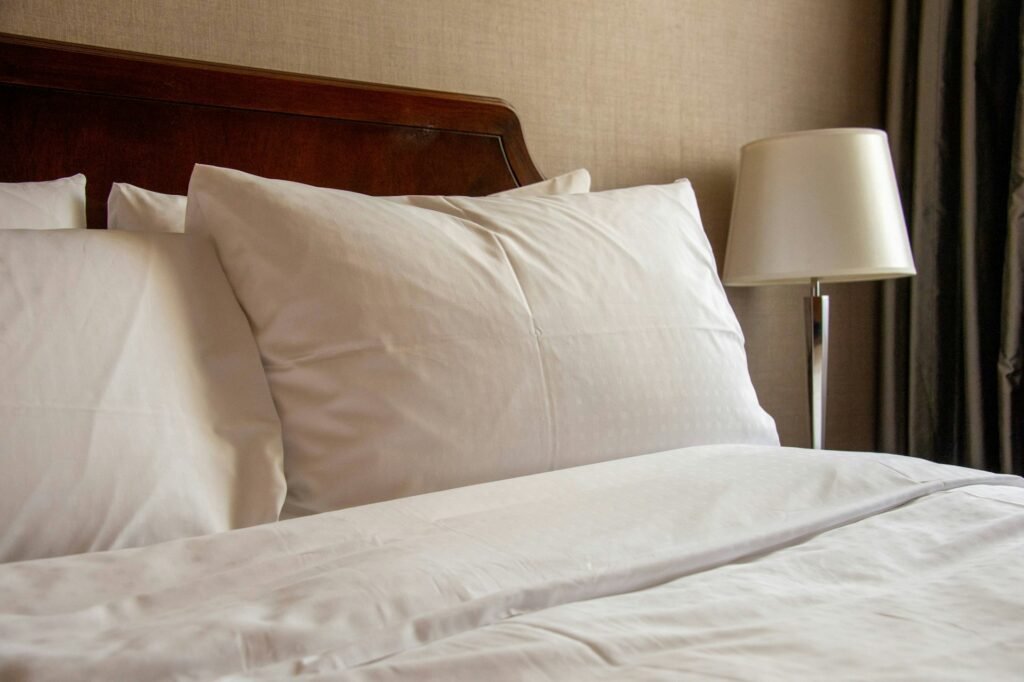 Close view of white pillows on a bed with a lamp beside it.