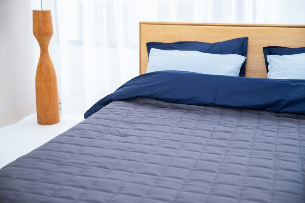 Bed with a blue comforter and pillows in a bright bedroom.