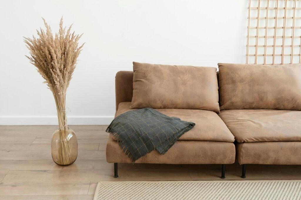 Sofa with a knit throw blanket and dried pampas in a bright room.