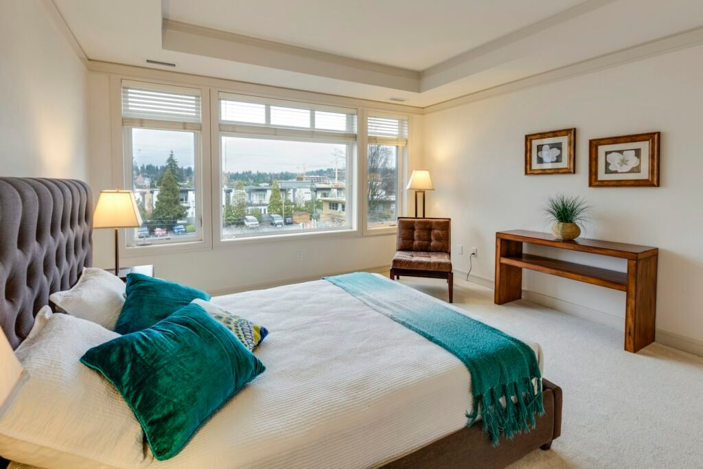 Bright bedroom with a neatly made bed, white sheets and teal pillows.