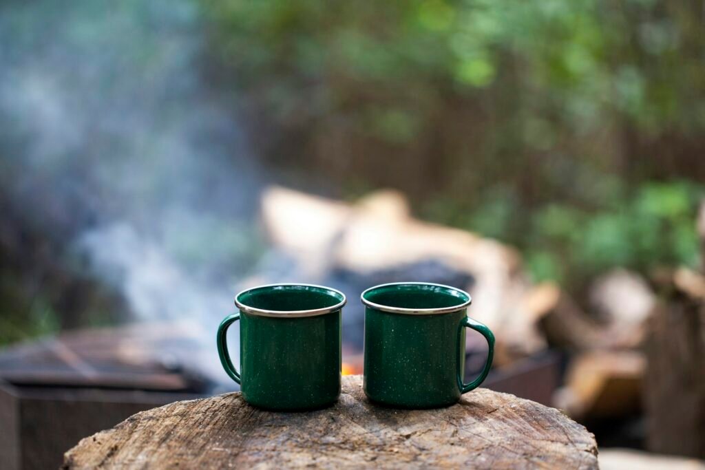 Two green enamel mugs on a log beside a campfire.