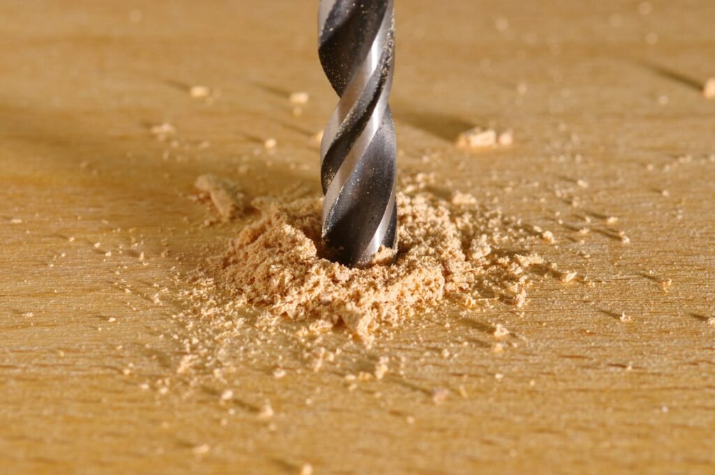 Drill bit boring into a wooden board with fine sawdust.