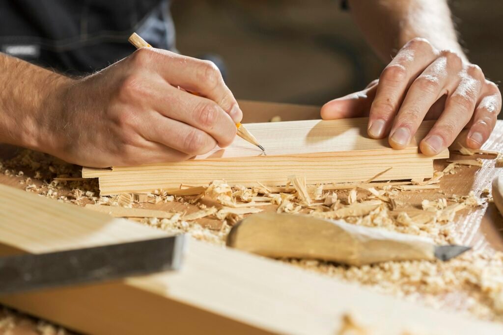 Hands marking a line on a wooden board in a woodworking shop.