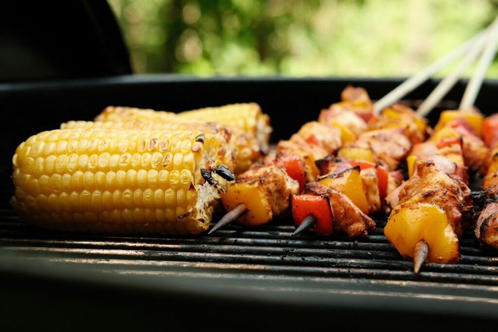 Corn on the cob and skewers cooking on a grill.