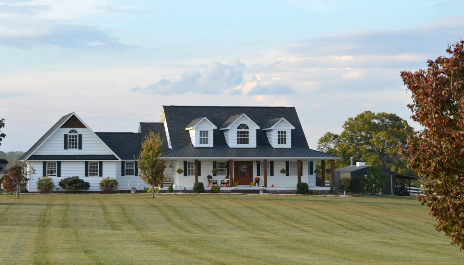 White farmhouse with a wraparound porch and a striped green lawn