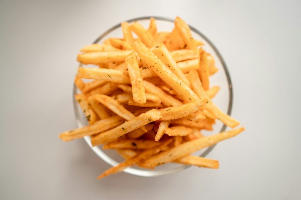 Golden french fries in a clear bowl on a light background.