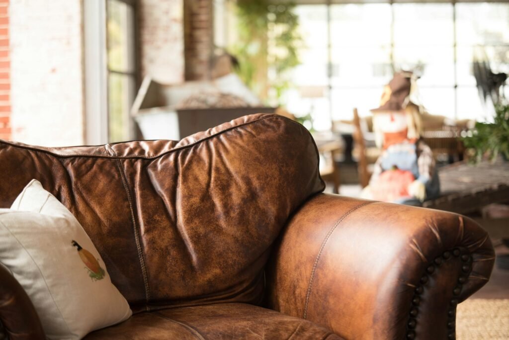 Brown leather armchair with pillows by a sunny window.