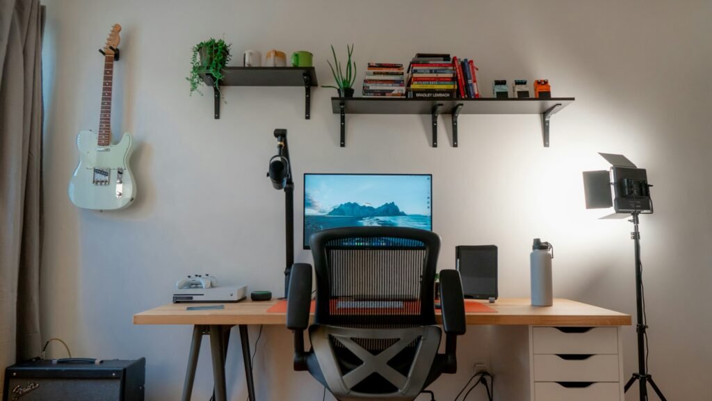 Home office desk with a monitor, shelves and a guitar on the wall.