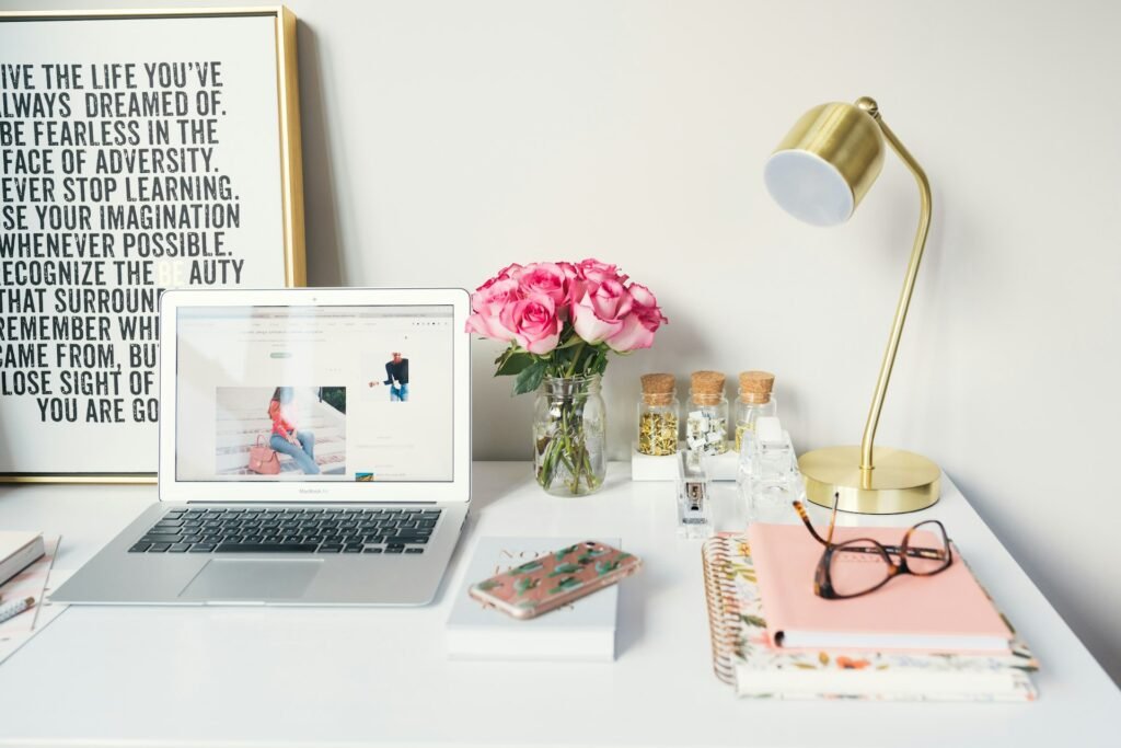 Bright white desk with a laptop, flowers and a lamp.