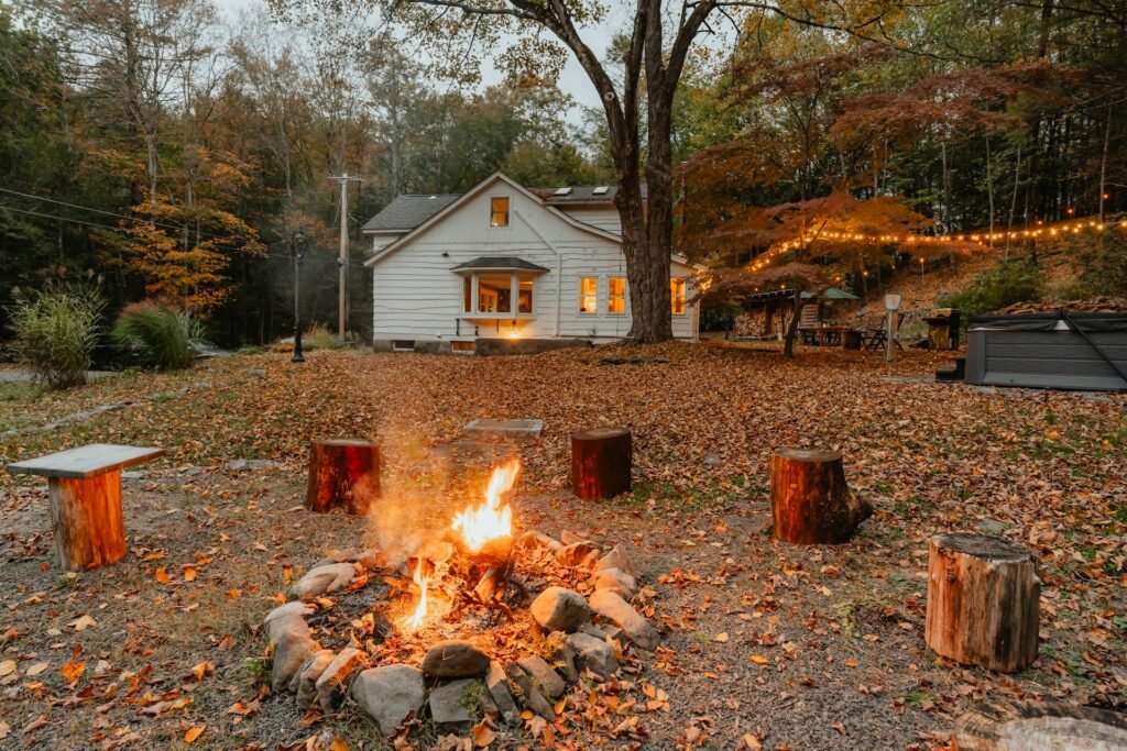 Backyard fire pit with a white house and autumn leaves.