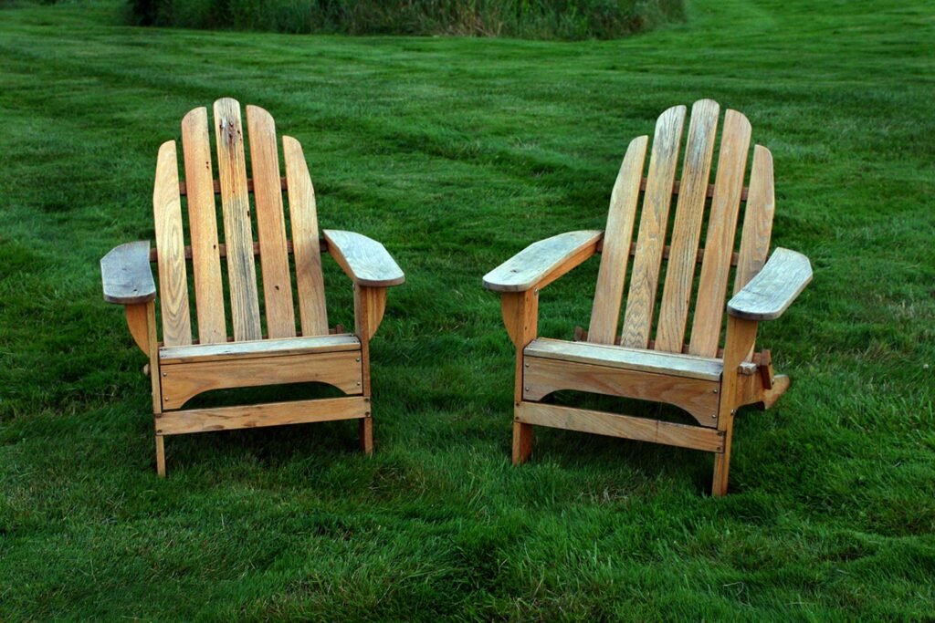 Two wooden Adirondack chairs on a green lawn.
