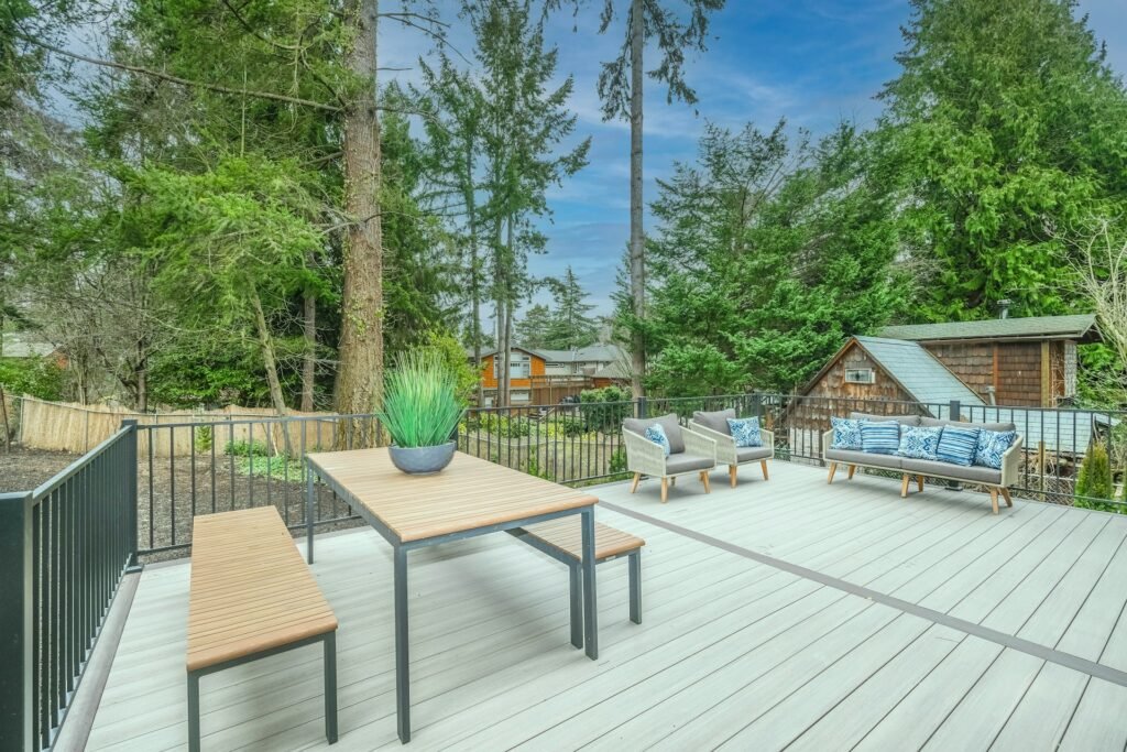 Wooden deck with a dining table and chairs in a leafy backyard.