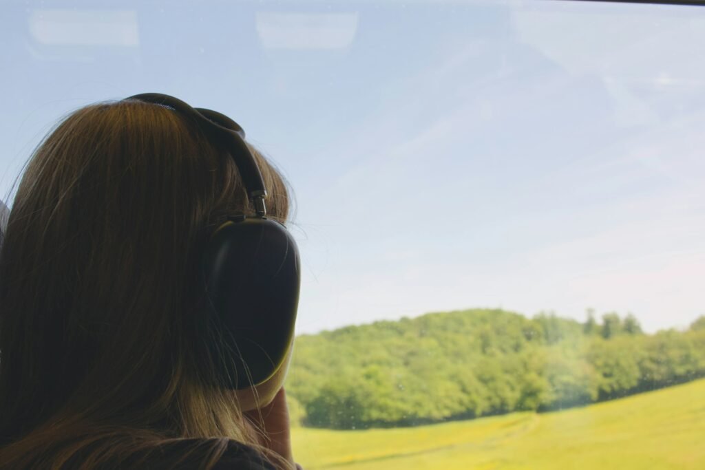 Traveler wearing headphones looking out a train window at green hills.