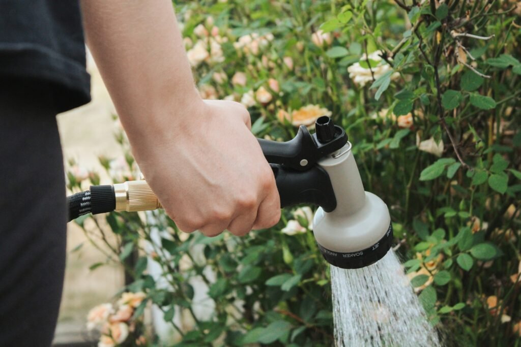 Hand holding a hose nozzle watering garden plants.